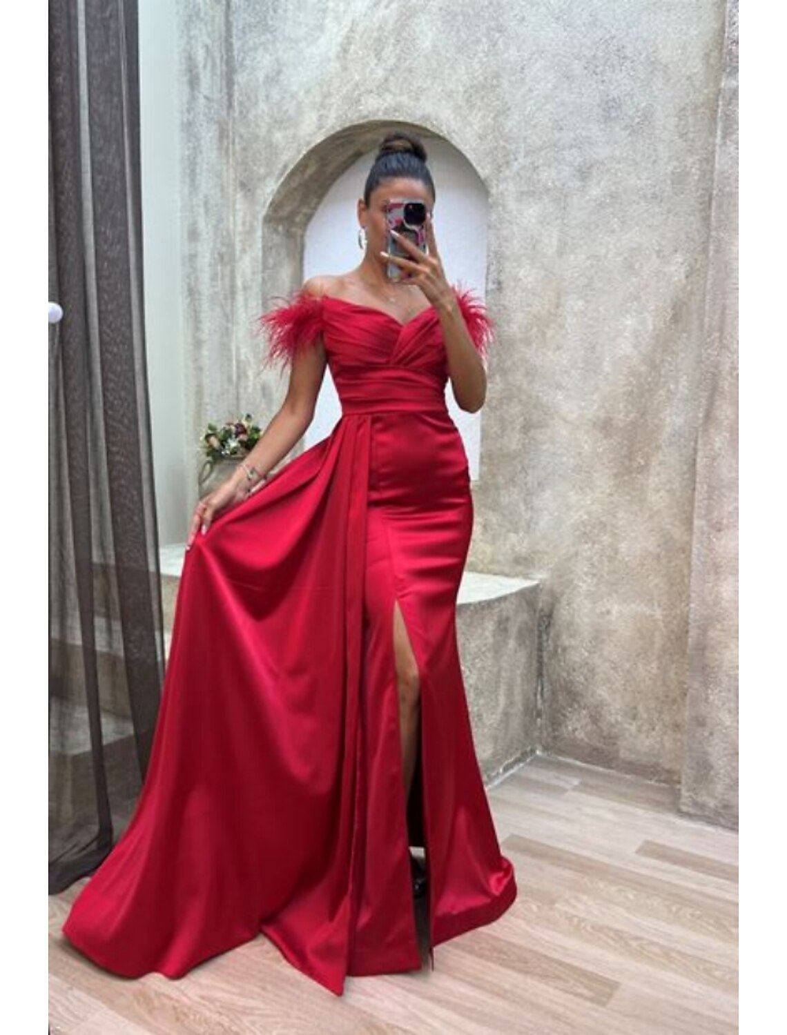 Model wearing a chic A-line off-shoulder satin gown with high slit and feathers.