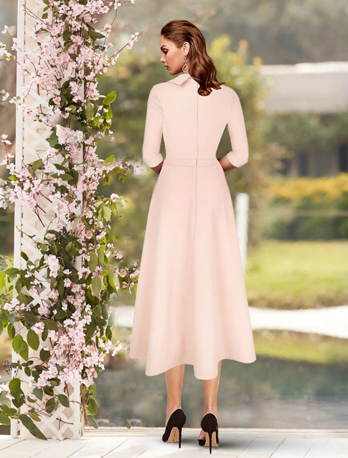 Woman posing in a light-colored tea length sheath dress with pleats and 3/4 sleeves.