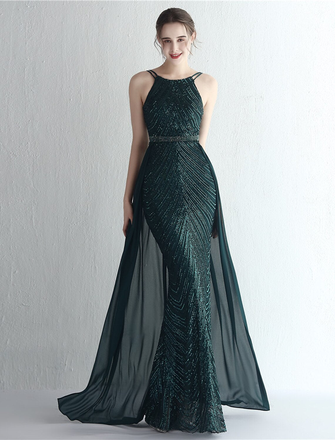 Full view of a woman in a shimmering halter neck floor-length dress.